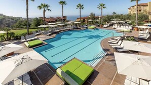 Un'area piscina con sedie a sdraio e ombrelloni, circondata da palme e edifici.