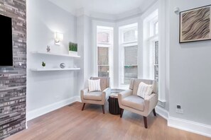 A modern living room with two armchairs, a coffee table, and a fireplace. There are white shelves with decorative items and a framed picture on the wall. - Gold Coast Pristine 5BR - 3.5BA - Patio - Parking (Chicago)