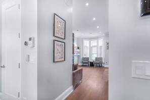Un couloir aux murs blancs, orné de deux œuvres d’art abstraites encadrées, avec un banc en bois et un coin salon composé de deux fauteuils.