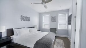 A modern bedroom with a bed, bedside tables, a ceiling fan, and a window with blinds. - Gold Coast Pristine 5BR - 3.5BA - Patio - Parking (Chicago)