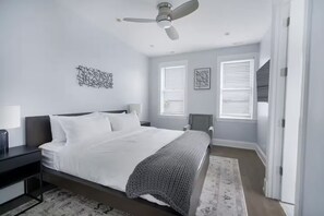 Une chambre moderne avec un lit, des tables de chevet, un ventilateur de plafond et une fenêtre avec des stores.
