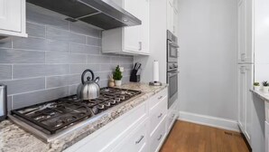 A modern kitchen with white cabinets, a stainless steel range hood, a gas stove, and a microwave. - Gold Coast Pristine 5BR - 3.5BA - Patio - Parking (Chicago)