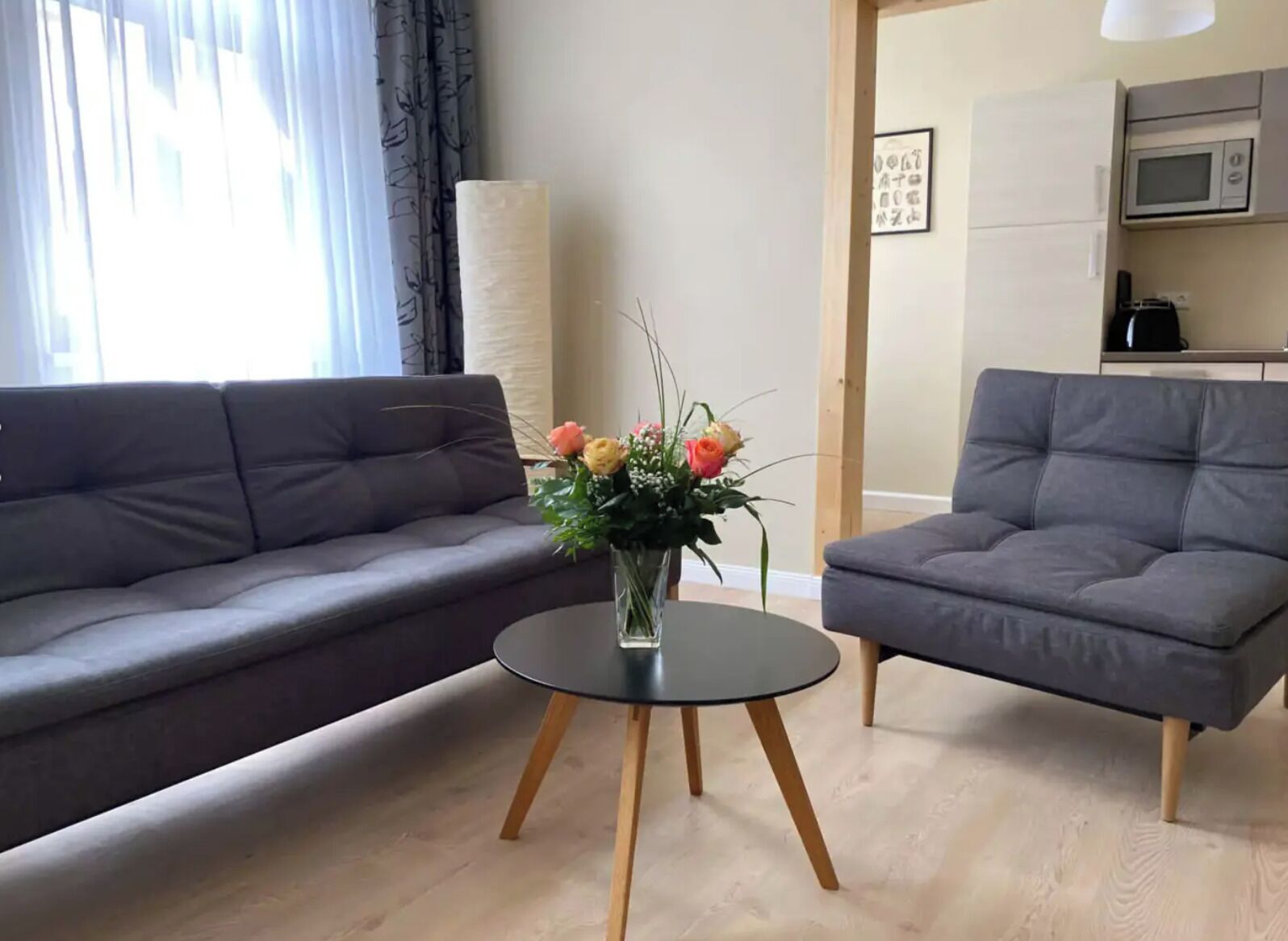 Ein Wohnzimmer mit grauem Sofa, einem runden Tisch mit Blumenvase und einem grauen Sessel.