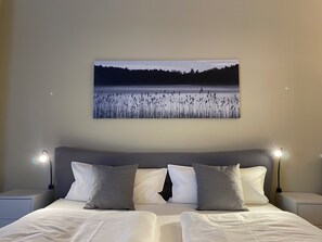 A bedroom with a bed, two bedside tables, a nightstand, and a wall-mounted picture of a landscape. - Ferienwohnungen Bautzen (Bautzen)