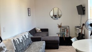 A modern living room with a sectional sofa, a dining table, a flat-screen TV, and a mirror on the wall.