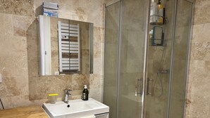 A bathroom with a glass shower enclosure, a sink with a soap dispenser, and a towel hanging on a cabinet.