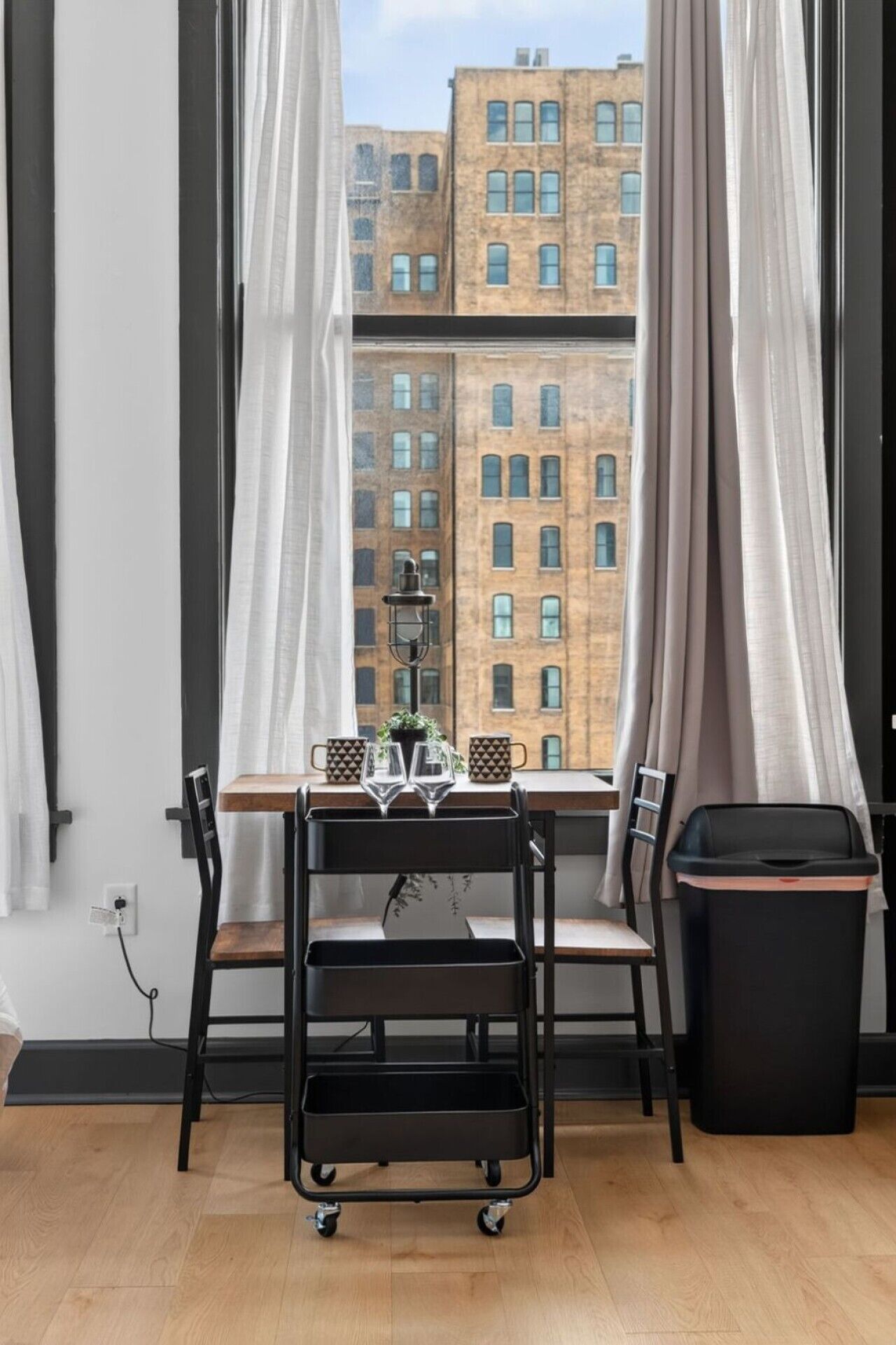 A room with a dining table, chairs, a small cart, and a trash bin.