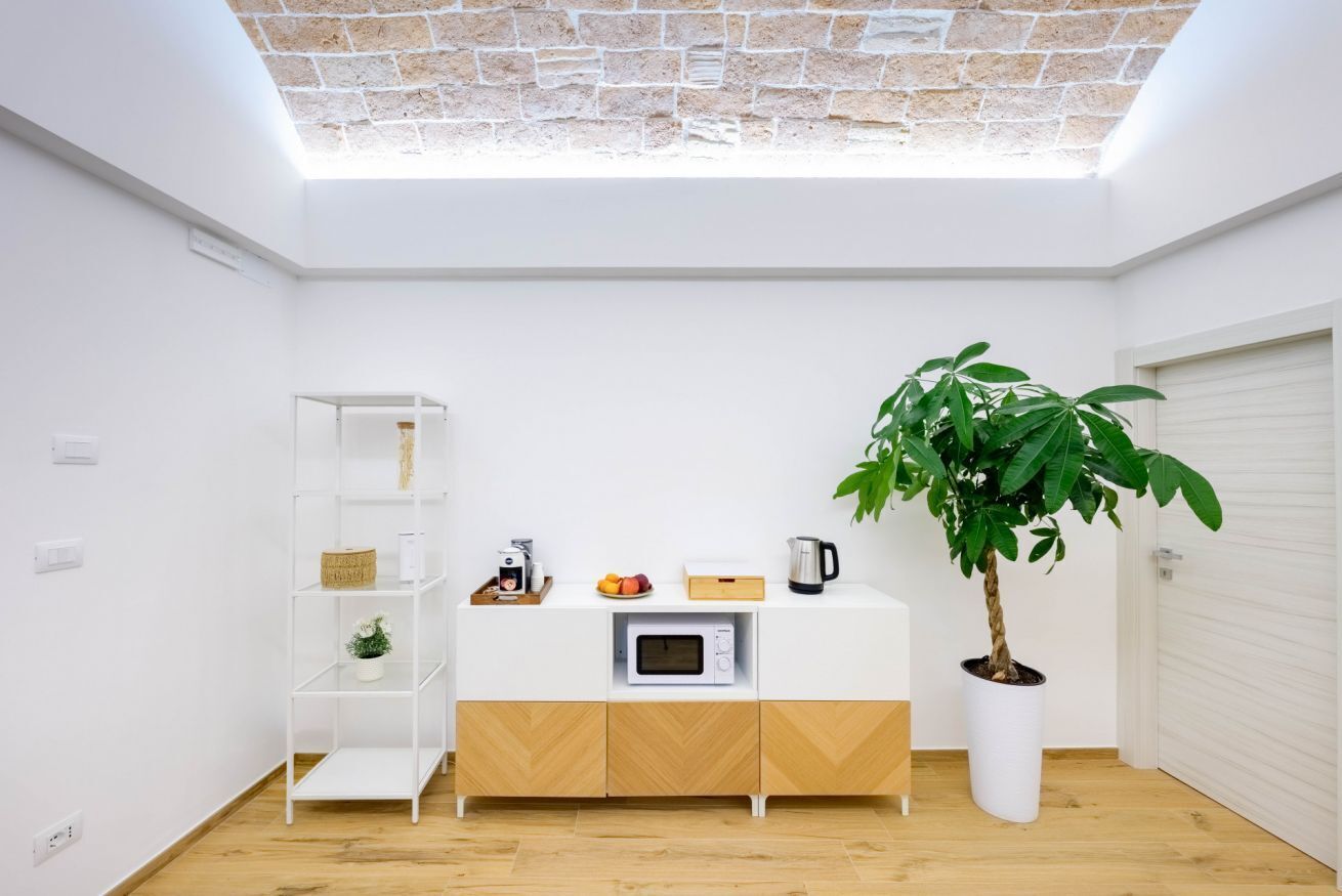 Una cucina moderna con un piano di lavoro bianco, un forno a microonde, una macchina da caffè e una pianta in vaso.
