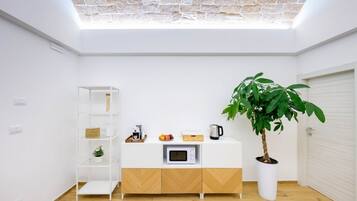 Una cucina moderna con un piano di lavoro bianco, un forno a microonde, una macchina da caffè e una pianta in vaso.