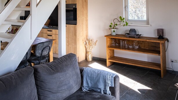 Et moderne interiør med trappe, sofa, konsolbord i træ og et vindue med persienner.