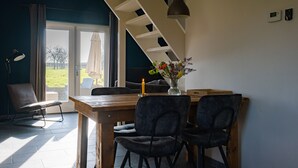 En spiseplads med et træbord, mørke stole, en vase med blomster, en hængende pendellampe og udsigt gennem en glasdør.