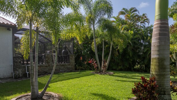En välskött trädgård med ett varierat utbud av träd och buskar, en gång av sten och en byggnad med ett tak täckt av tegelpannor.
