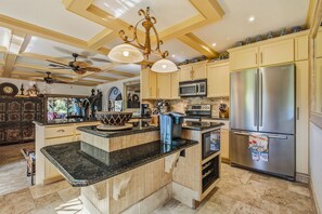 A kitchen with a central island, stainless steel appliances, wooden cabinets, and a ceiling fan. - Private Serene Florida Estate Near Beaches (Fort Myers)