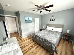 A bedroom with a bed, a ceiling fan, a nightstand, a wall-mounted lamp, a painting, and a door. - 1 Block to the Beach - 4BR - Fenced Yard - Sleeps 8 - Port Clinton - Lake Erie (Port Clinton)