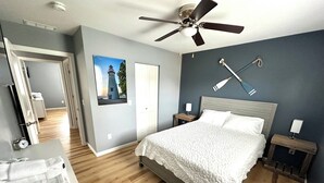 A bedroom with a bed, a ceiling fan, a nightstand, a wall-mounted lamp, and a door leading to another room. - 1 Block to the Beach - 4BR - Fenced Yard - Sleeps 8 - Port Clinton - Lake Erie (Port Clinton)