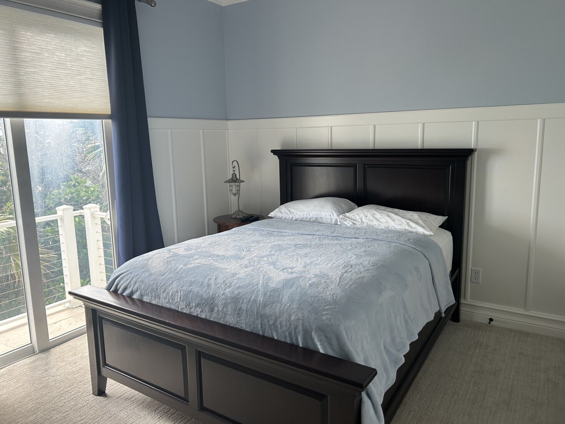 Une chambre à coucher avec un lit, une table de chevet, une lampe et une vue sur l’extérieur.