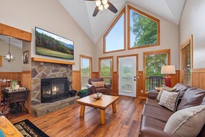 A spacious living room with a stone fireplace, a television mounted on the wall, and large windows providing natural light. - Welcome to Biltmore Escape, your perfect Sevierville retreat nestled in the hear (Sevierville)