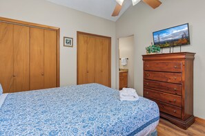 Un dormitorio con cama, armario de madera, cómoda y televisor en la pared.