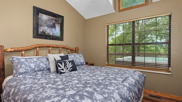 A bedroom with a wooden headboard, a large window with blinds, a framed picture on the wall, and a bed with patterned bedding. - Welcome to Biltmore Escape, your perfect Sevierville retreat nestled in the hear (Sevierville)