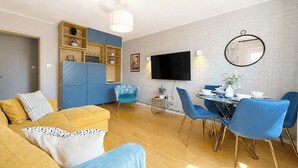 Ein modernes Wohnzimmer mit einer Couch, einem Esstisch mit Stühlen, einem Fernseher und einem Bücherregal.
