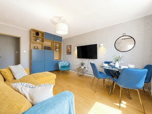 Ein modernes Wohnzimmer mit einer Couch, einem Esstisch mit Stühlen, einem Fernseher und einem Bücherregal.