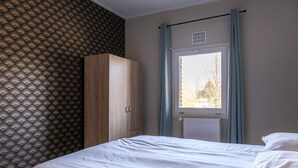 Un dormitorio con cama, armario, ventana con cortinas y radiador.