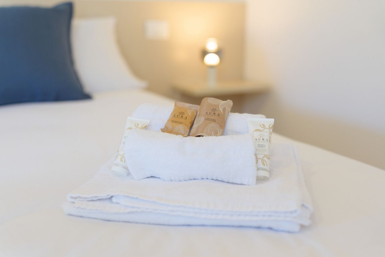 A neatly made bed with a folded white towel and two small brown packages on top.