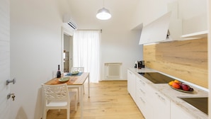 Une cuisine compacte avec des meubles blancs, un plan de travail en bois et un luminaire suspendu.