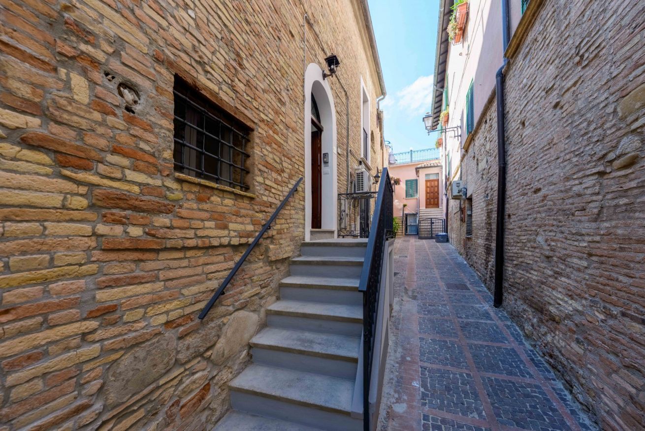 A narrow alleyway with stone walls, a set of stairs, and a small door at the top.