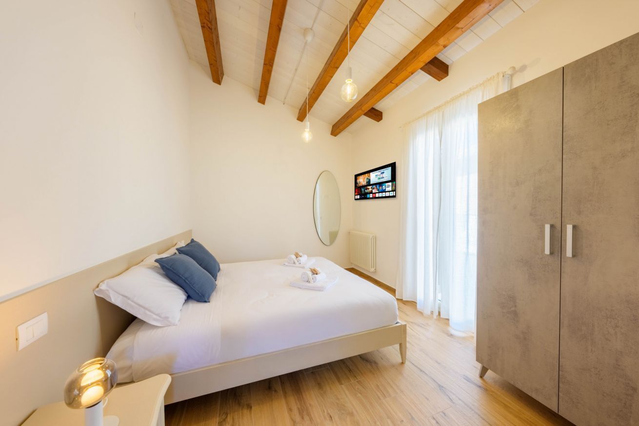Een slaapkamer met een bed, nachtkastje, houten balken, een kledingkast en een televisie aan de muur.