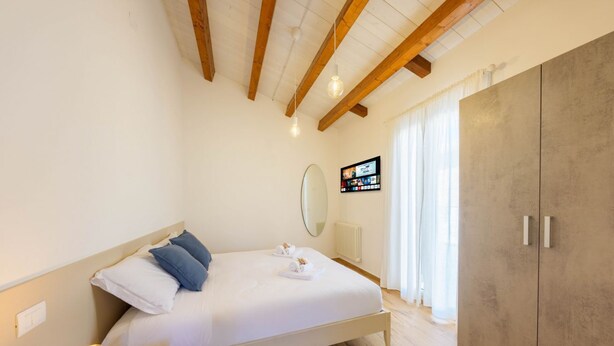 Une chambre à coucher avec un lit, une table de chevet, des poutres en bois, une armoire et un téléviseur fixé au mur.