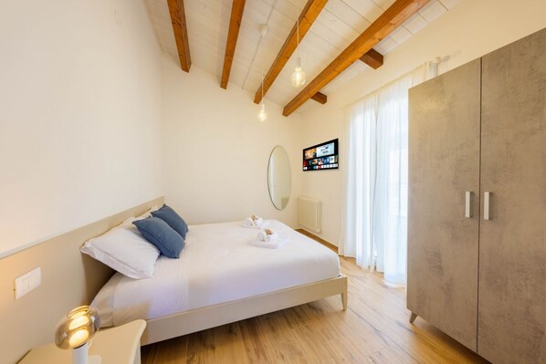 Ein Schlafzimmer mit Bett, Nachttisch, Holzbalken, Kleiderschrank und Fernseher an der Wand.