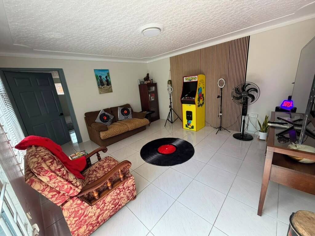 Una sala de estar con un sofá, una mesa de centro, un tocadiscos, un ventilador y una pequeña mesa con un teclado.
