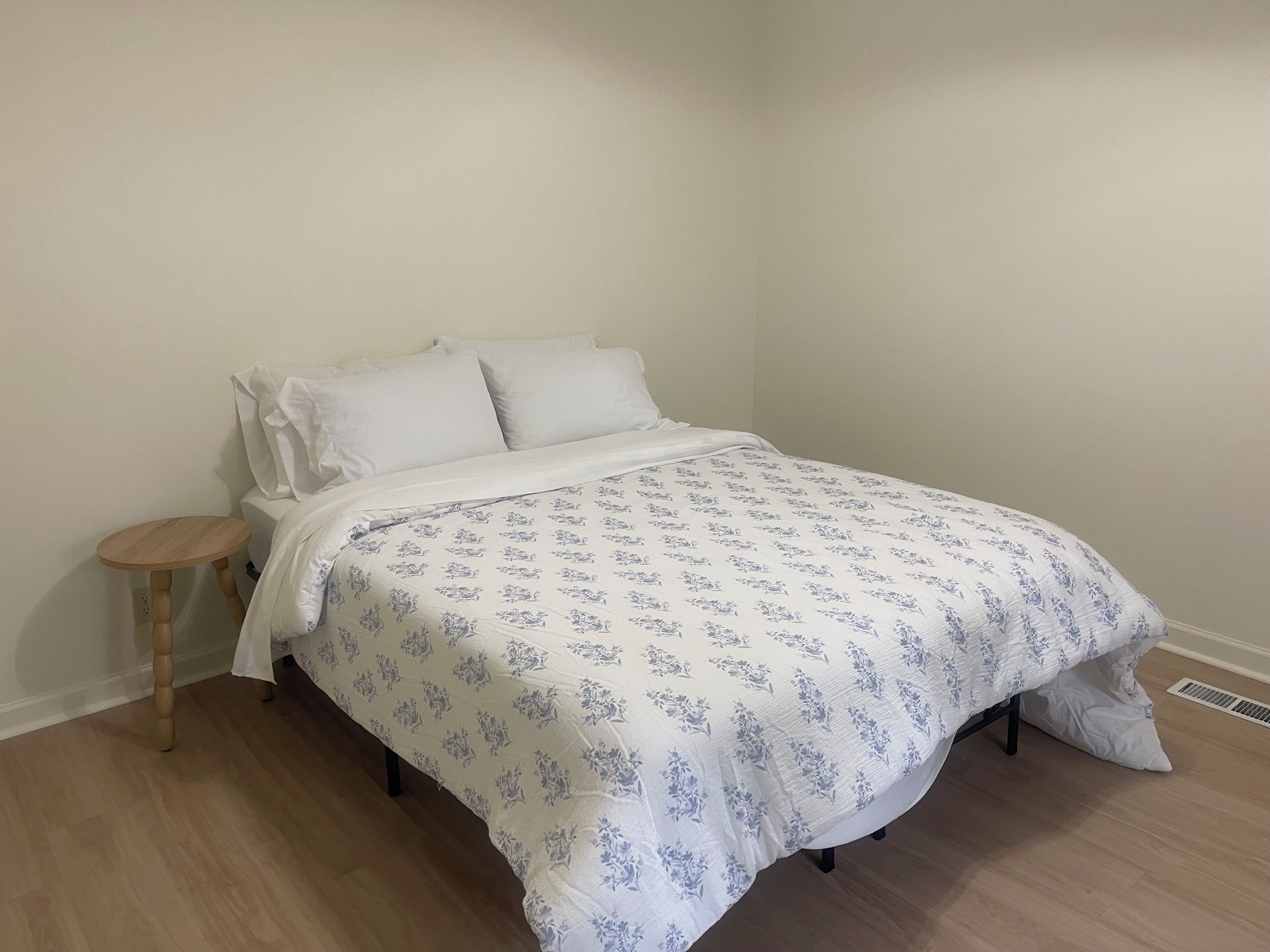 A single bed with a floral-patterned bedspread, a wooden nightstand, and a white wall.
