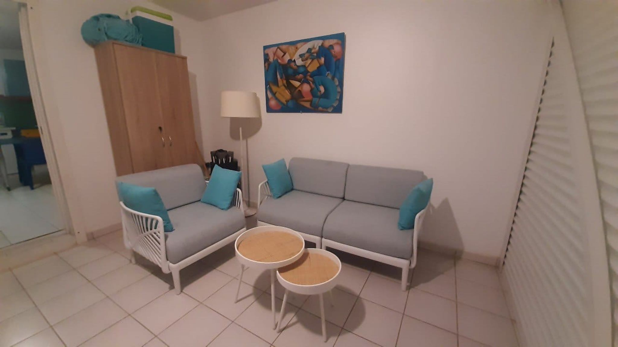 A living room with a grey sofa, two white chairs, a small round table, a lamp, and a painting on the wall.