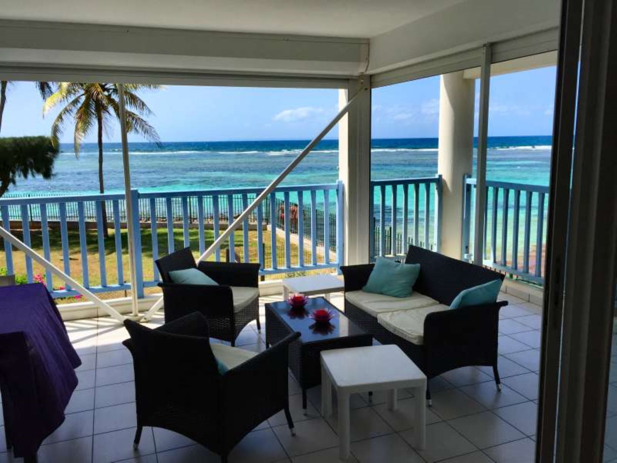 A balcony with a view of the ocean, furnished with a sofa, chairs, and a small table.