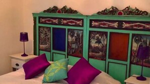 Cama com cobertura branca, duas almofadas roxas e uma almofada verde-água com design amarelo.