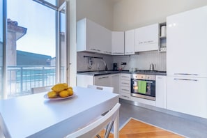 A modern kitchen with white cabinets, a dining table with a fruit bowl, and a view through a large window. - 5 minutes from the M5 Metro station, Università Bicocca, with a private garage (Milano)