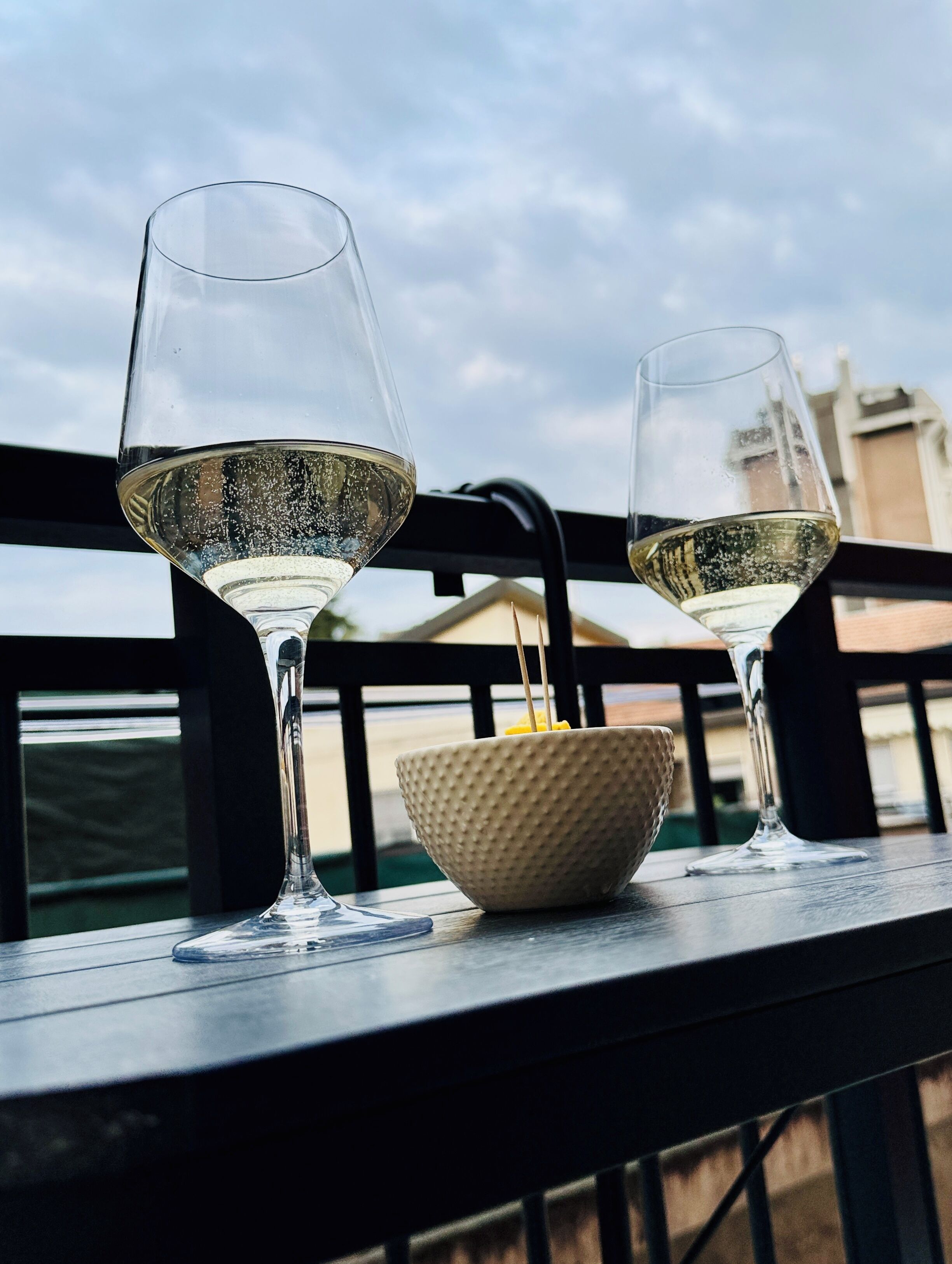Two wine glasses on a balcony railing with a bowl in between.