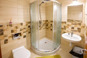 A bathroom with a glass-enclosed shower, a white sink, and a toilet.