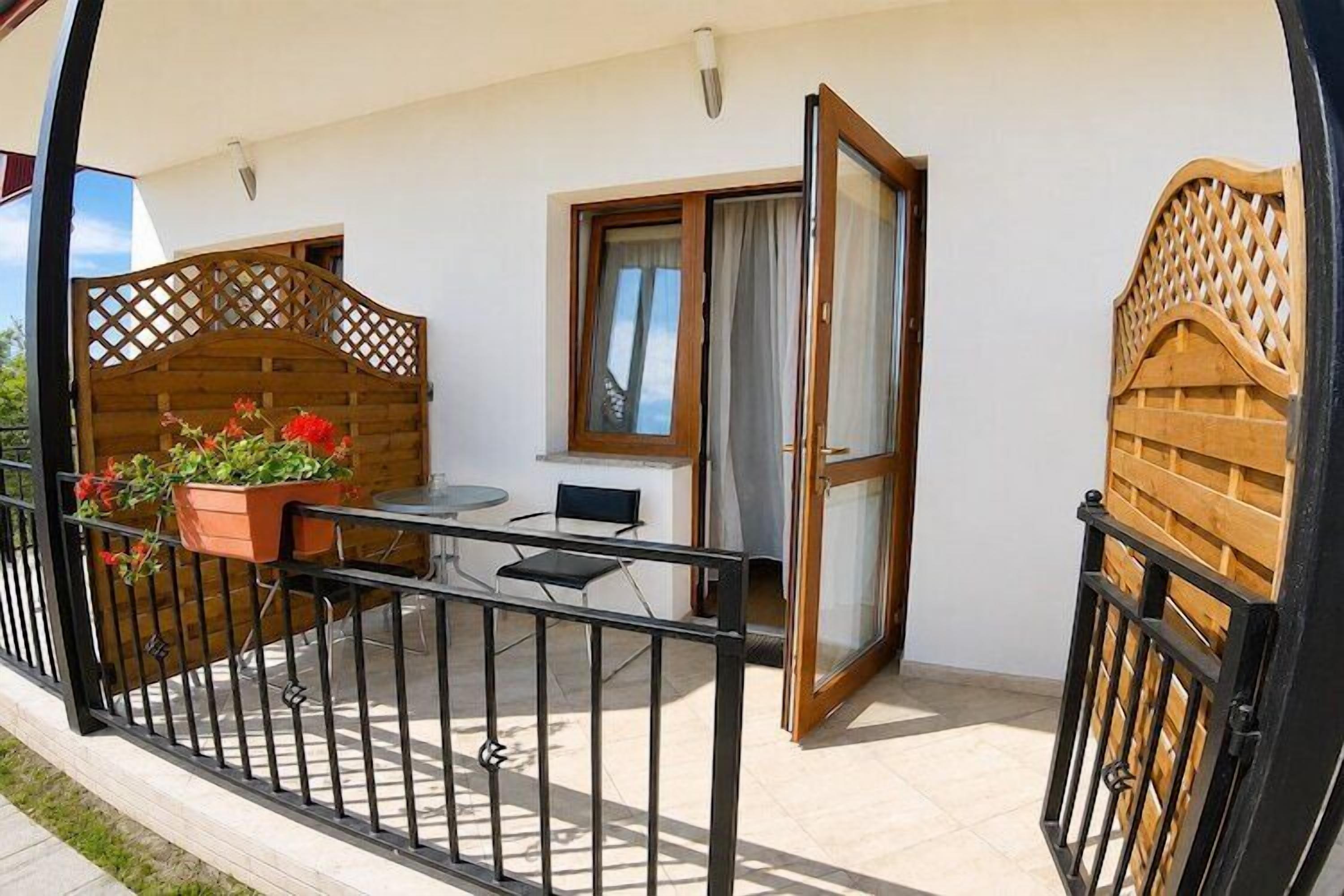 Un balcon avec une table et des chaises, une clôture en bois et une fenêtre avec des rideaux.