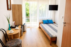 A room with a bed, a desk, a chair, a coffee maker, and a television.