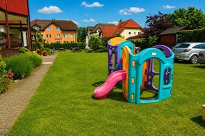 A playground with a slide and climbing structures in a residential area with houses and a clear sky.