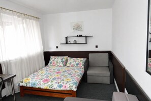 Ein Schlafzimmer mit einem Bett, einem Sessel, einem Schreibtisch und einem Regal mit Dekoration.