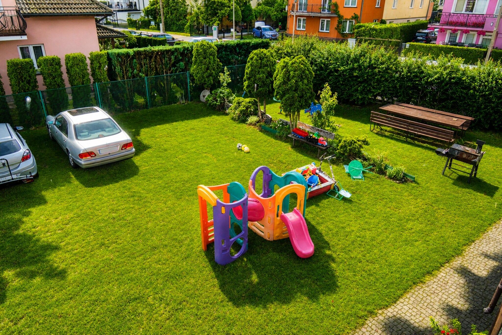 Un barrio residencial con un césped bien cuidado, juegos infantiles y coches aparcados.