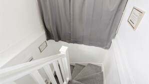 Un escalier avec une rampe blanche, des marches recouvertes d’un tapis gris et un rideau gris.