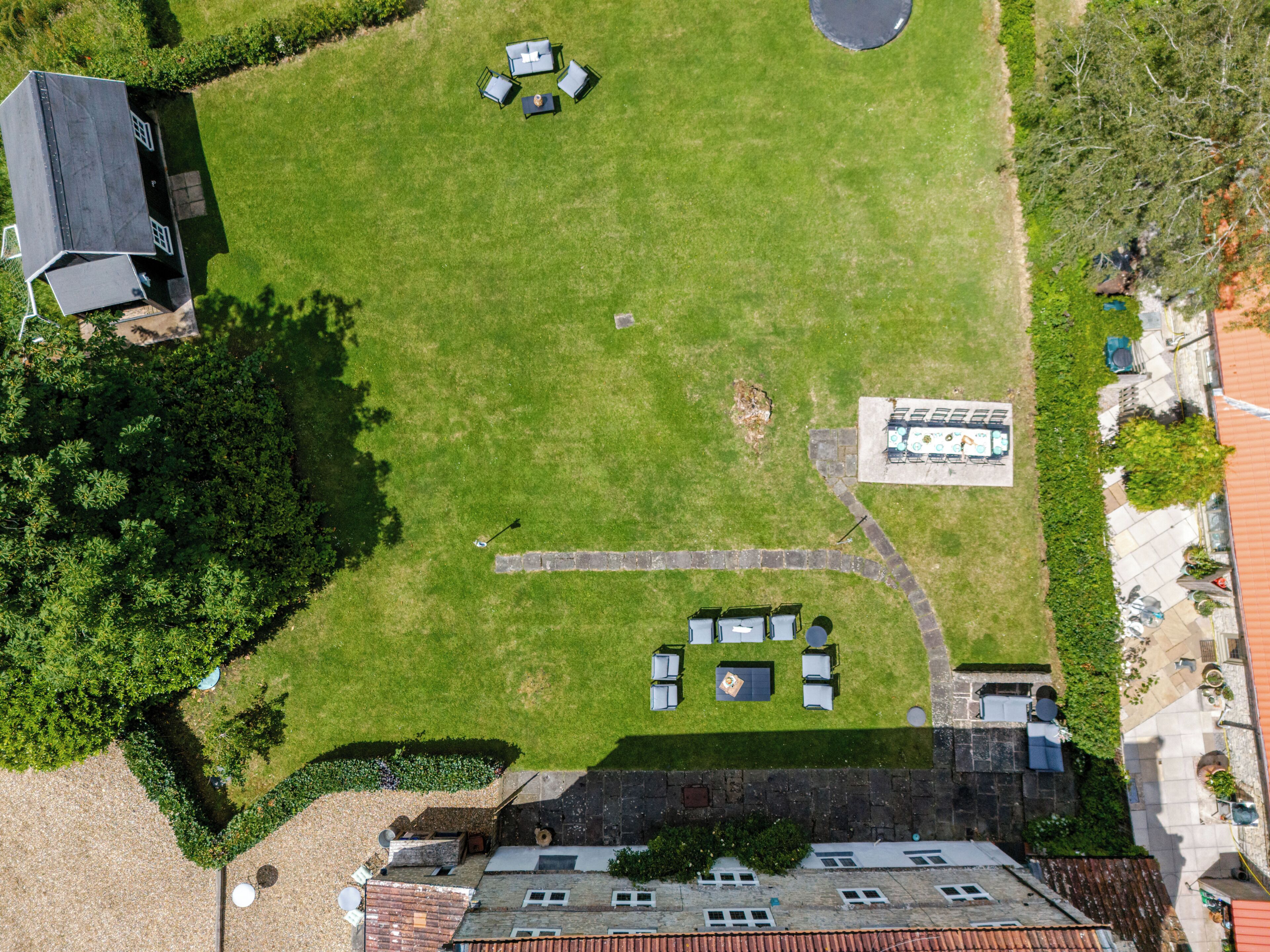 An aerial view of a property with a large lawn, outdoor seating area, and a stone pathway.