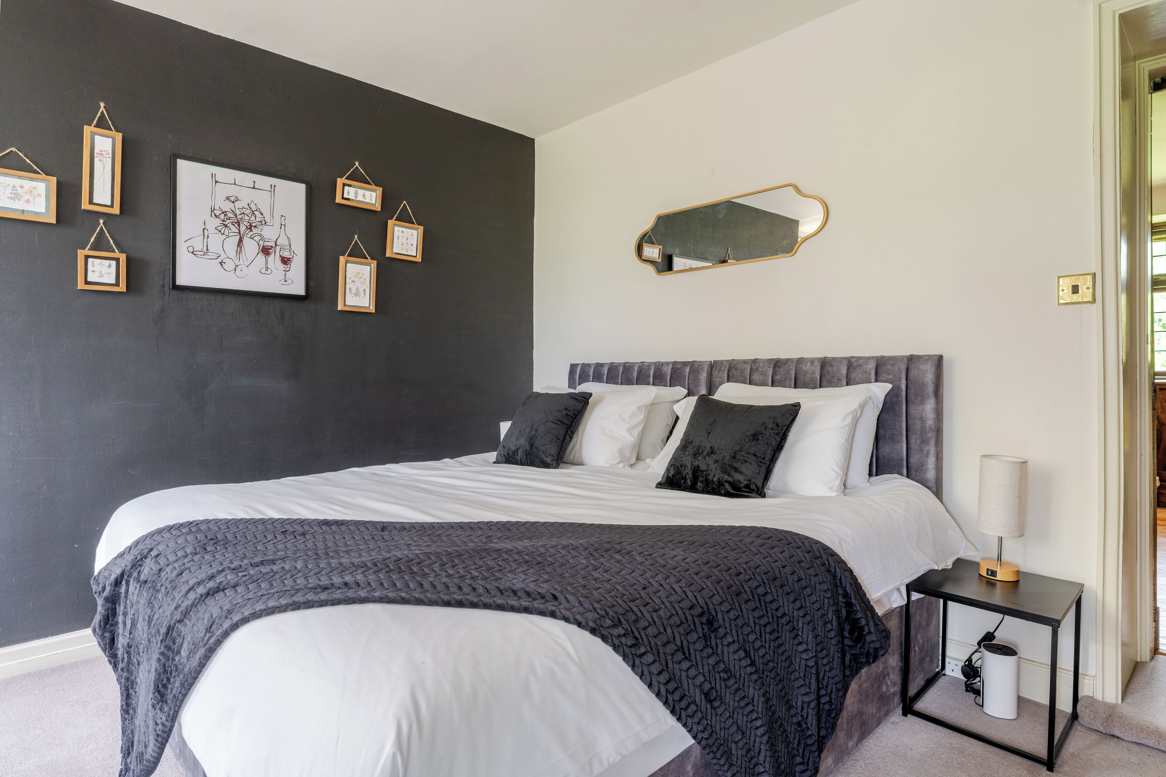 Un dormitorio con cama, mesita de noche, espejo en la pared y cuadro enmarcado.