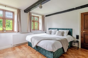 Un dormitorio con una cama, ventana, radiador, suelo de madera y una puerta.