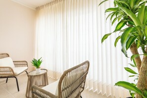 A room with a wicker chair, a small table with a plant, and a large window with sheer curtains. - View of Pontezuela (Santiago de los caballeros)